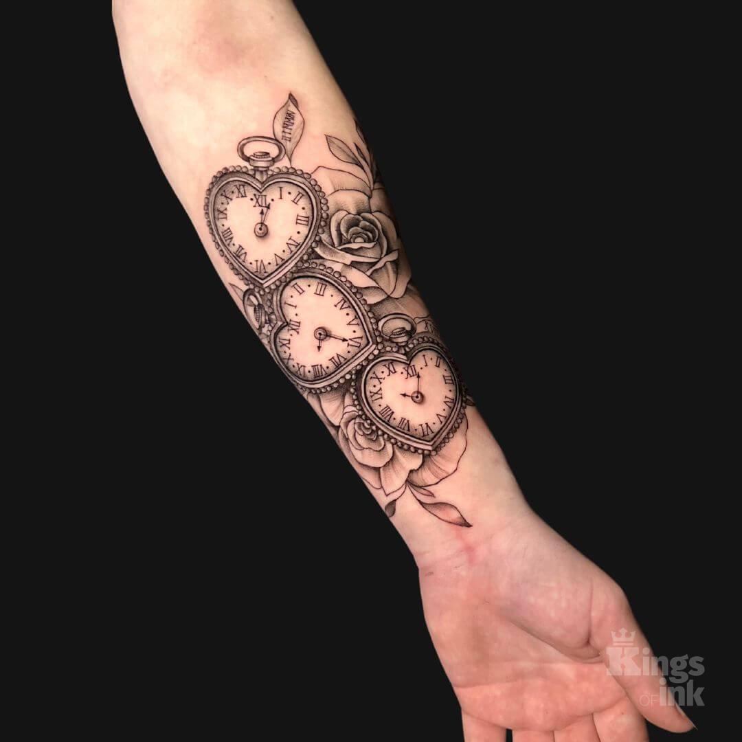 Trzy zegary w kształcie serce, wokół których znajdują się kwiaty.